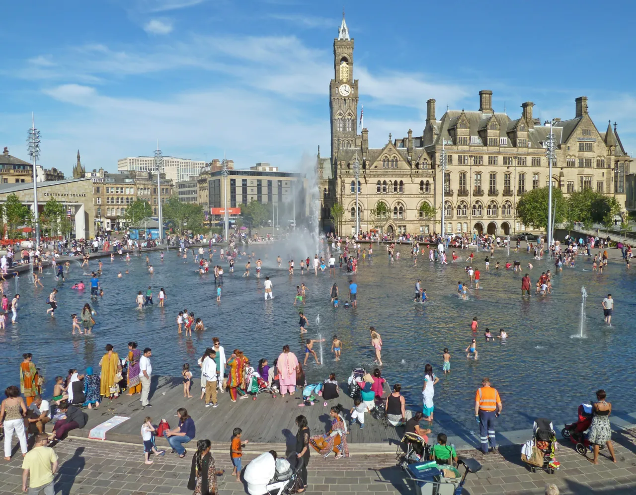 Crowds enjoying the mirror pool and fountains at Bradford City Park, highlighting inclusive urban design and public landscape architecture by Gillespies.
