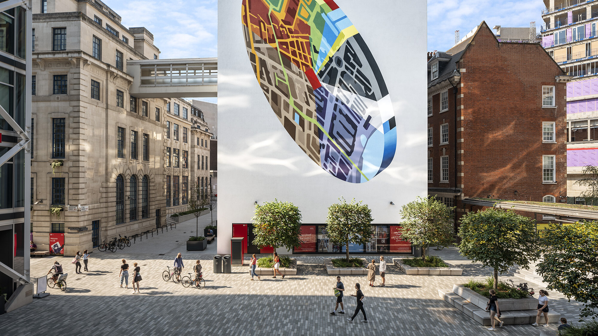 Colourful urban art mural overlooking public square with sculpted trees and integrated seating enhancing pedestrian-friendly public realm and landscape design at the entrance of LSE Centre Building.