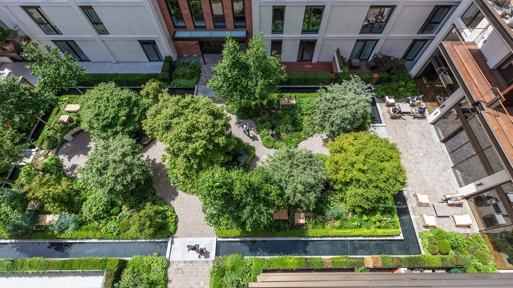 Luxury courtyard garden design with formal planting, paved walkways, and water features at Holland Park Villas.