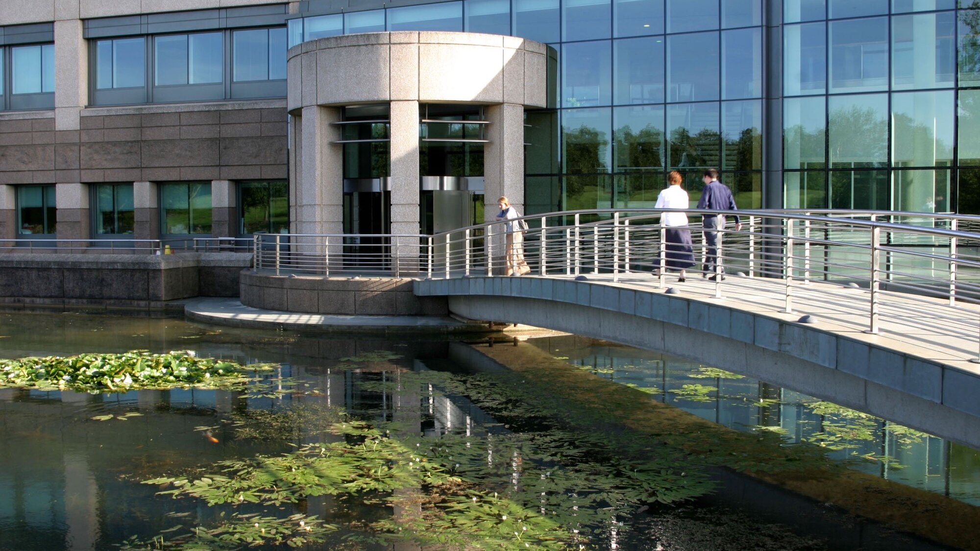Bridge over reflective pond at Glaxo Research Campus, Stevenage, showcasing sustainable corporate landscape architecture and water-sensitive design.