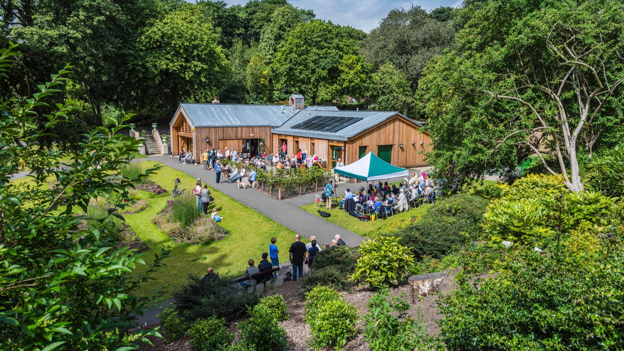 Community gathering at Northumberland Park visitor centre surrounded by landscaped gardens, oiutdoor seating, pathways, and mature trees.