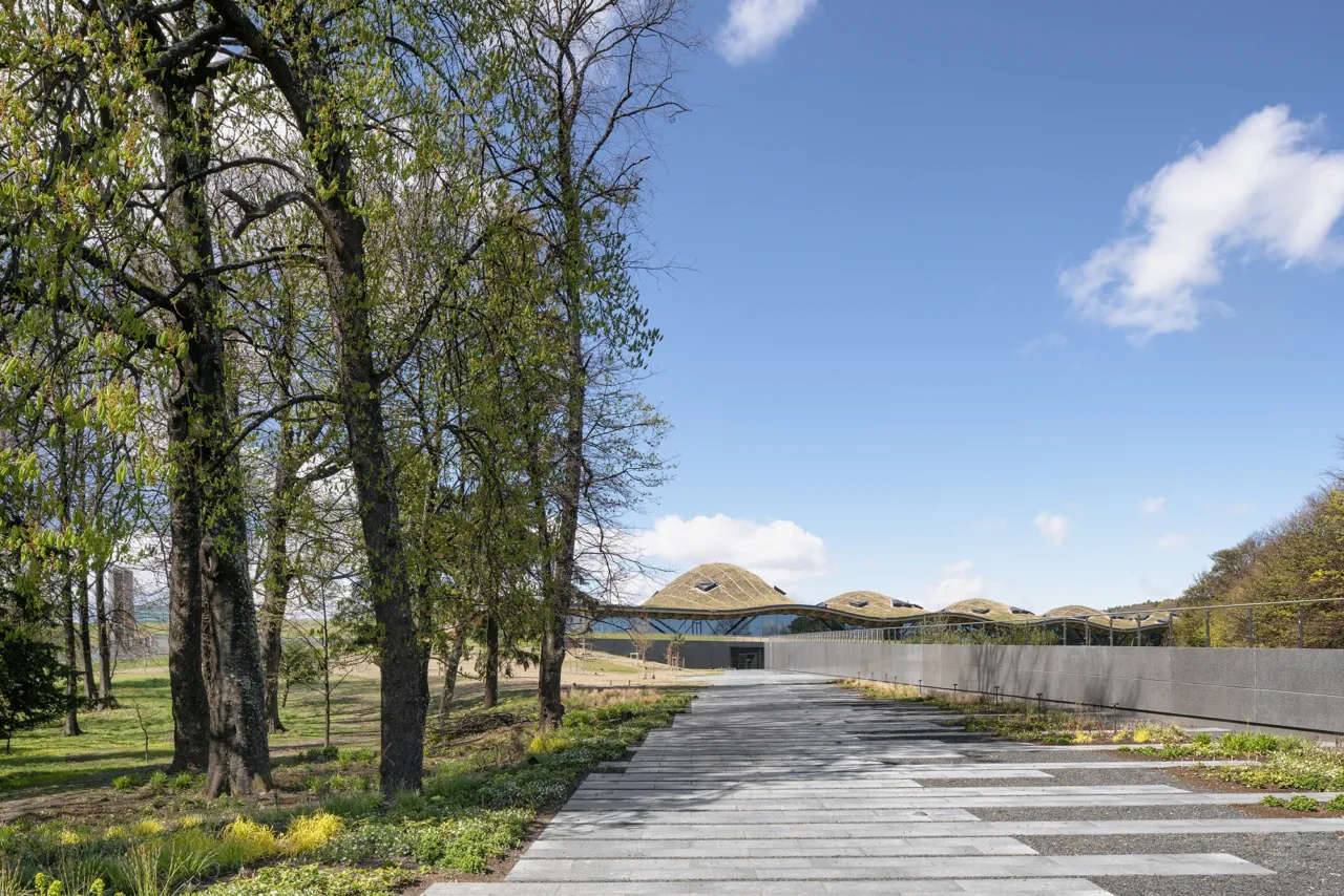 Entrance path to Macallan Distillery with green roof architecture blending into scenic Scottish landscape and surrounding woodland.