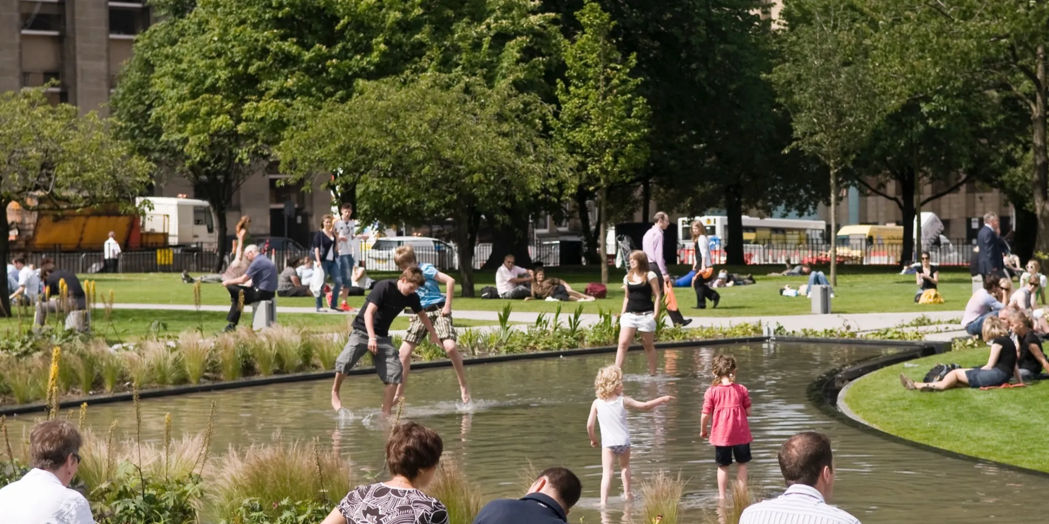 Children playing in the water feature at St Andrew Square, with surrounding seating, and interactive green space for public engagement in Edinburgh. Designed by landscape architecture practice Gillespies.