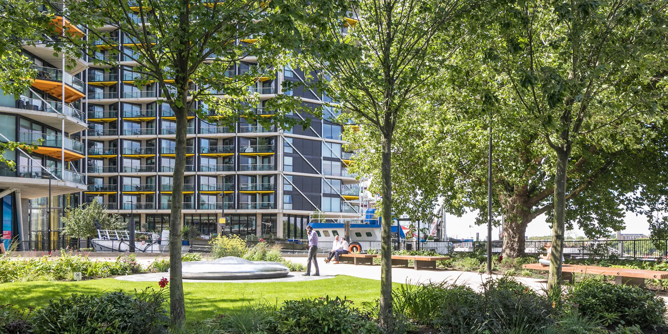 Riverlight residential landscape with mature trees, green lawns, and riverside public space in South London.