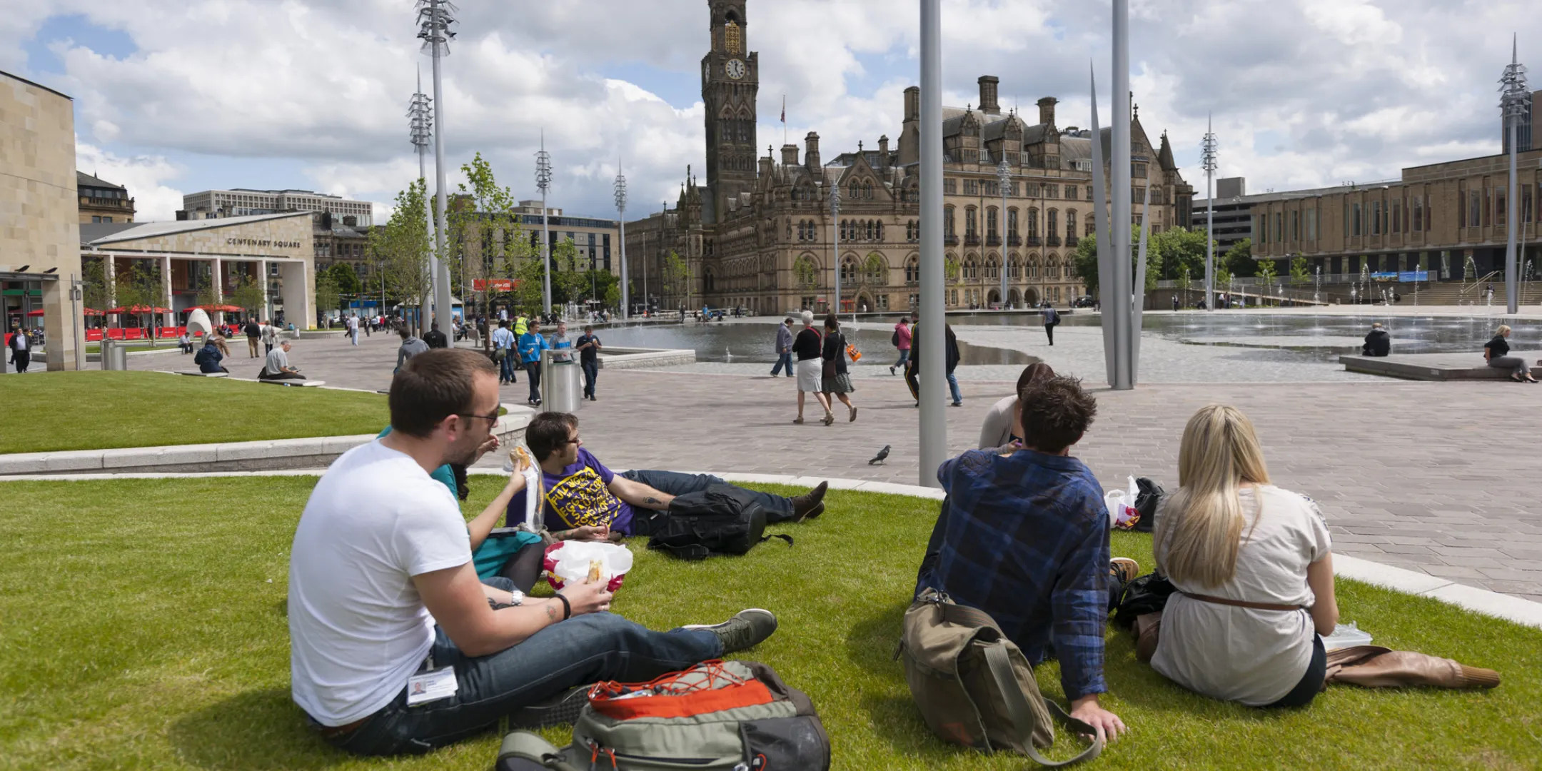 People relaxing on landscaped lawn at Bradford City Park, featuring sustainable green space and civic urban landscape design by Gillespies.