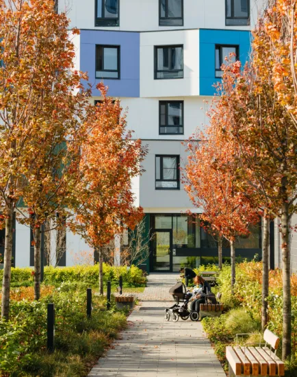 Colorful autumn planting and pathways at PIK Green Park Moscow with modern residential architecture in background.