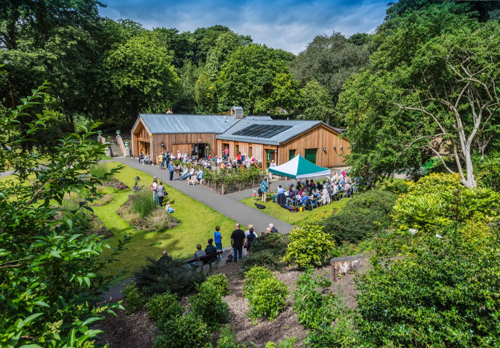 Community gathering at Northumberland Park visitor centre surrounded by landscaped gardens, oiutdoor seating, pathways, and mature trees.