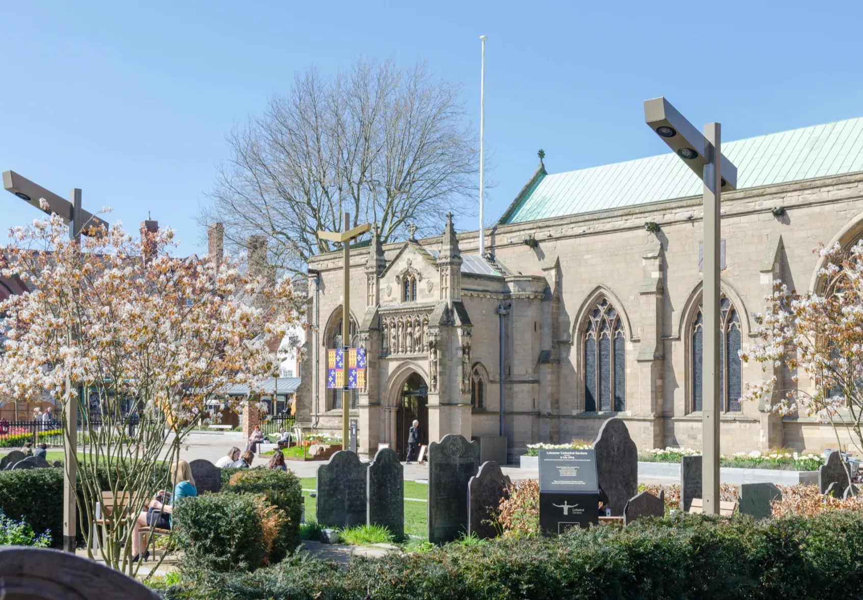 Leicester Cathedral Gardens landscape design with flowering trees, gravestones, heritage lighting, and public seating in spring.