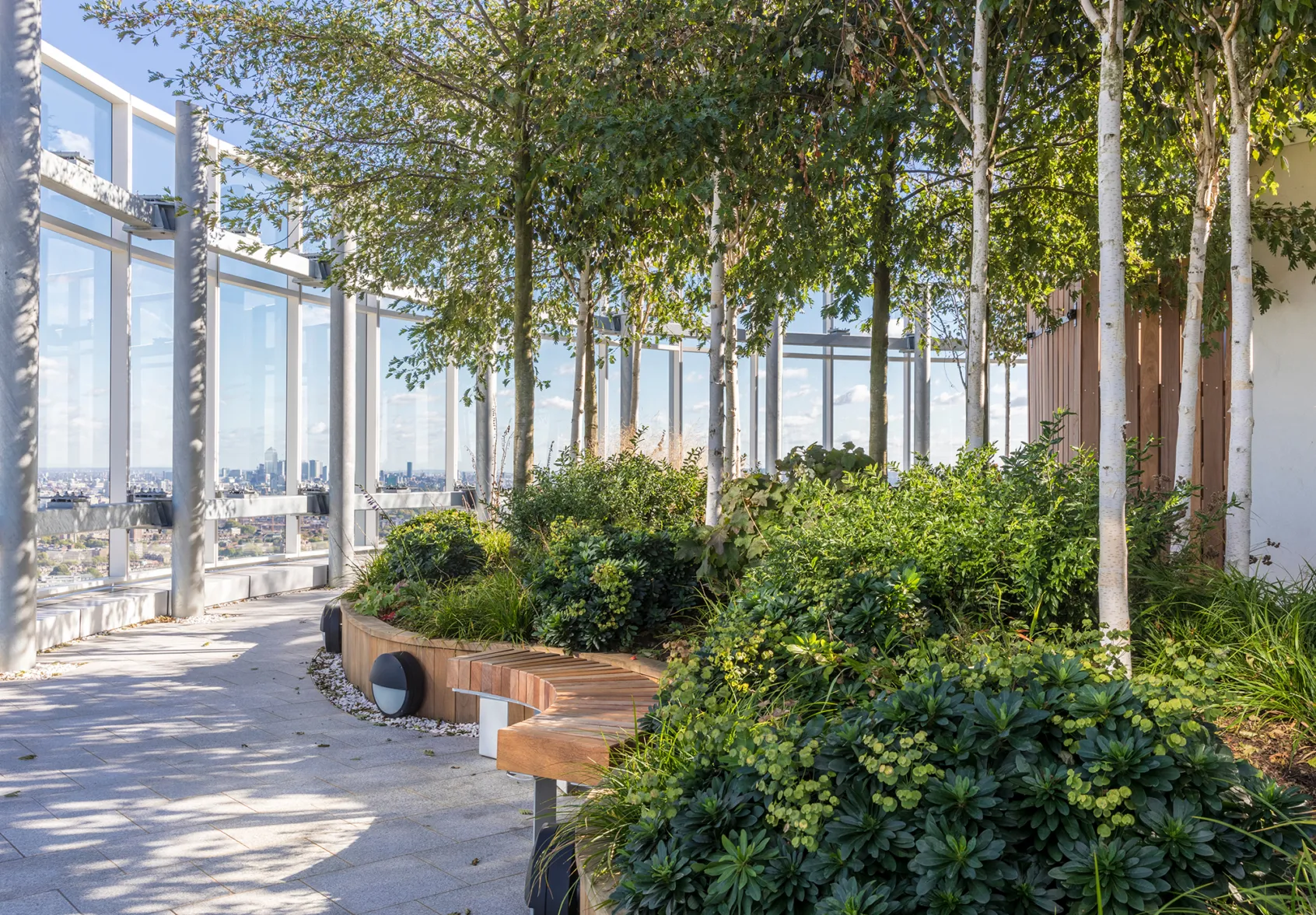 Vauxhall Sky Garden rooftop landscape with trees, planting, curved seating, and panoramic views of London skyline.