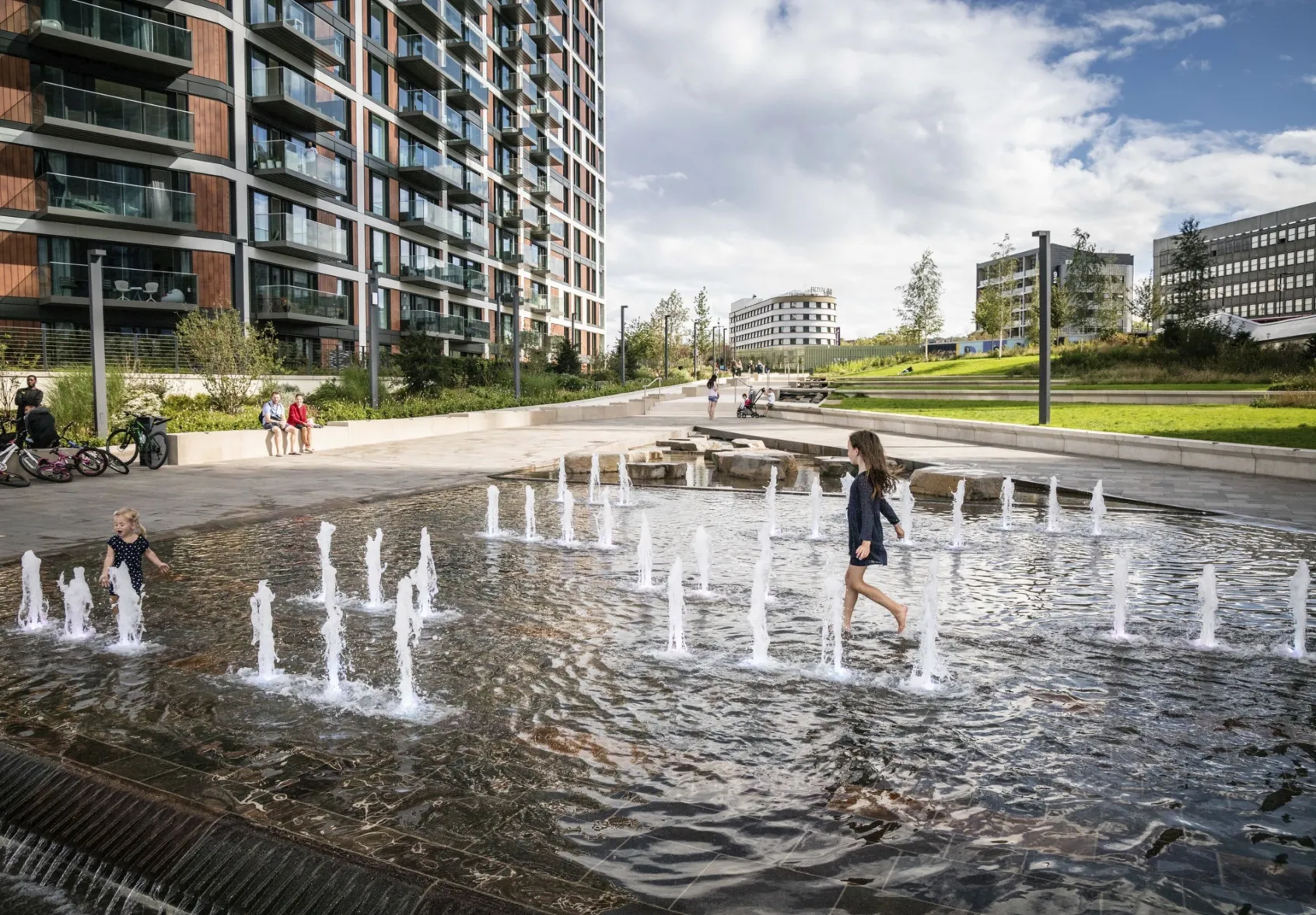 Children playing in interactive water fountain at Royal Arsenal Riverside waterfront urban landscape design.