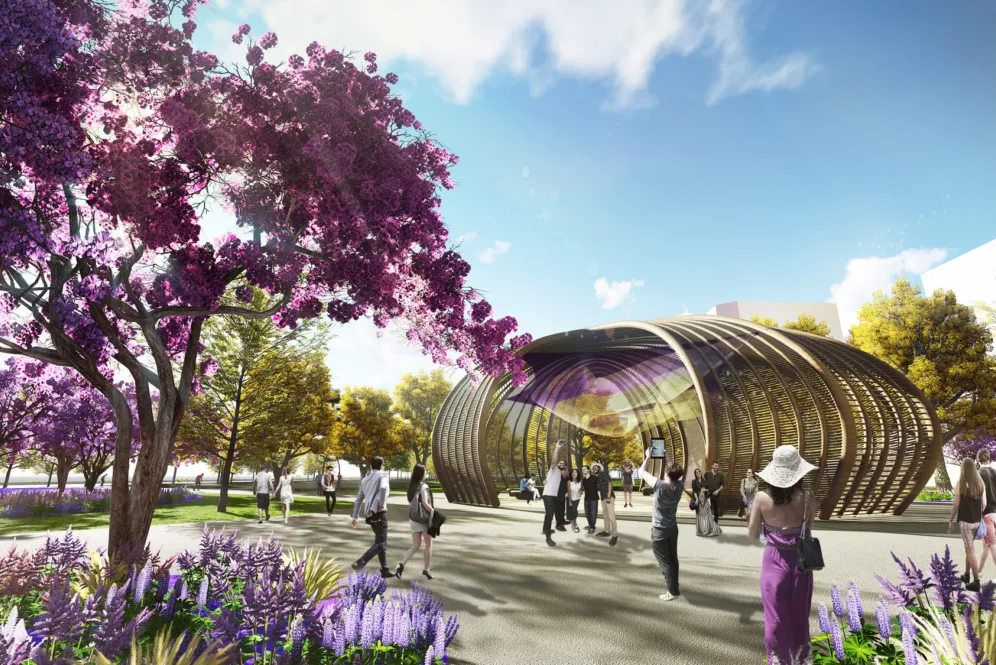 A sculptural timber pavilion set among flowering trees and vibrant planting, creating a welcoming civic focal point within the park.