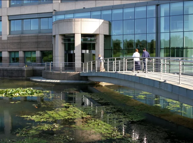 Bridge over reflective pond at Glaxo Research Campus, Stevenage, showcasing sustainable corporate landscape architecture and water-sensitive design.
