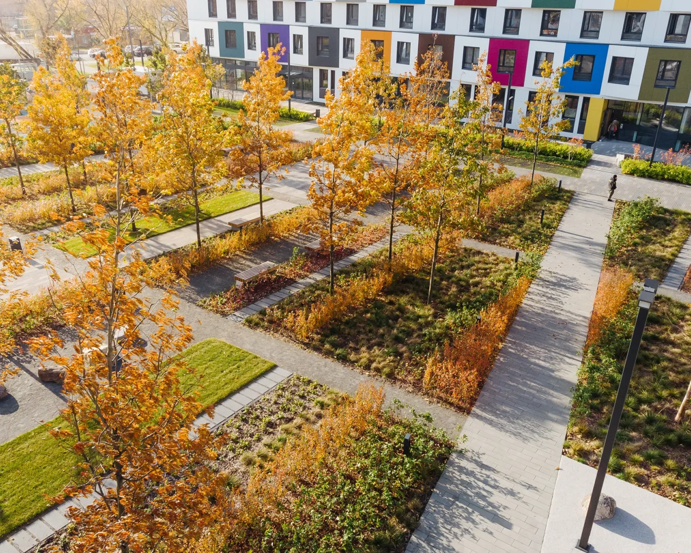 Colorful autumn planting and pathways at PIK Green Park Moscow with modern residential architecture in background.