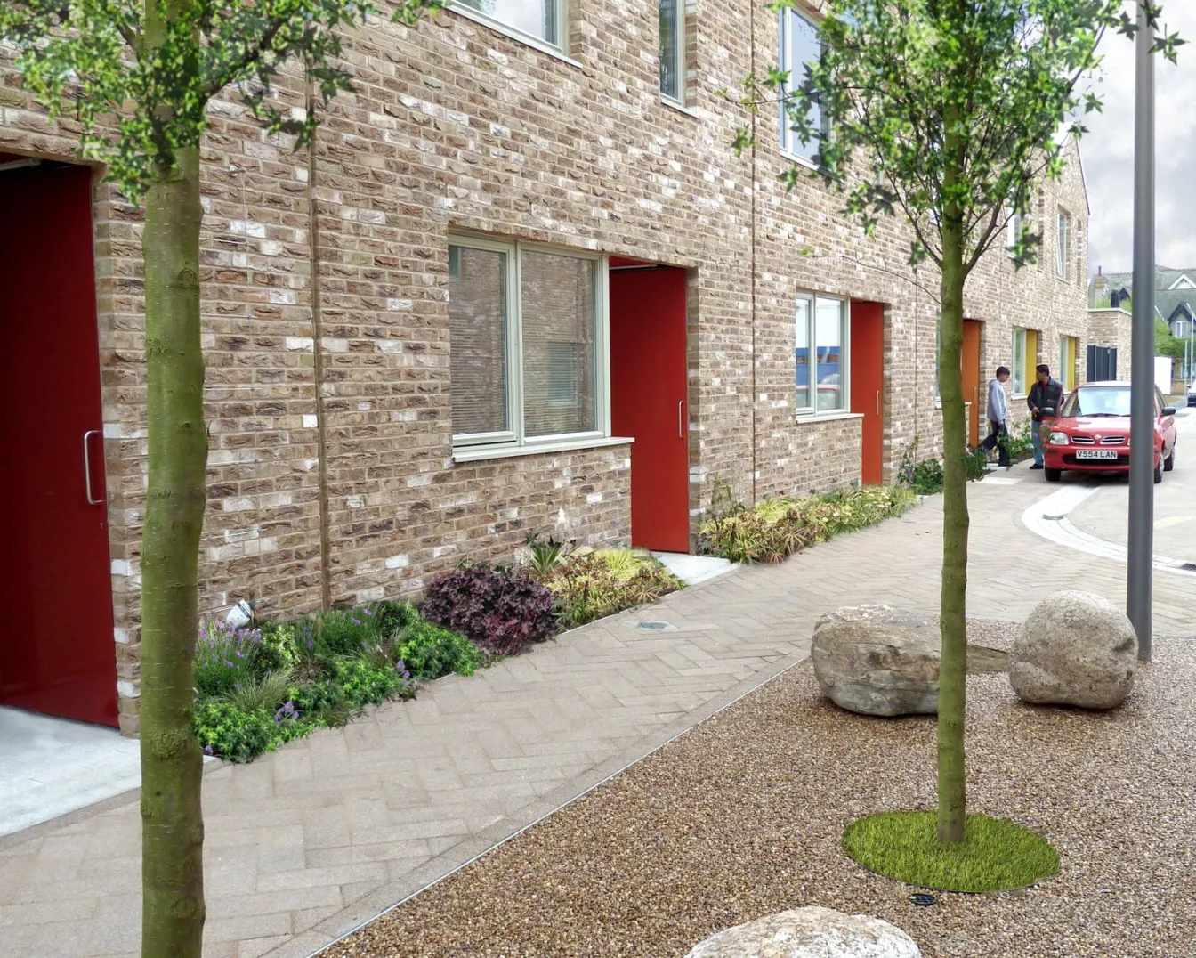 Shared residential streetscape at Anne Mews Barking with sustainable urban drainage, street trees, soft landscaping, and natural stone detailing.