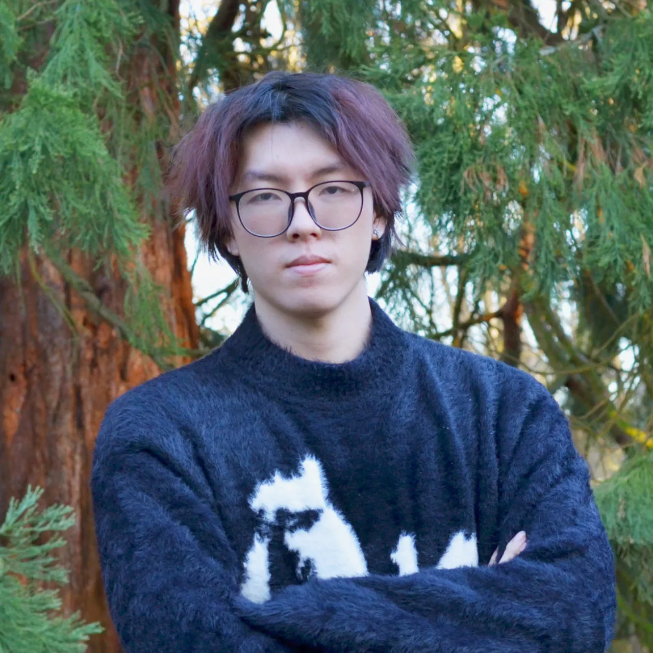 Zixuan Zhu, a young Graduate Landscape Architect at Gillespies, standing with his arms crossed in a woodland setting.
