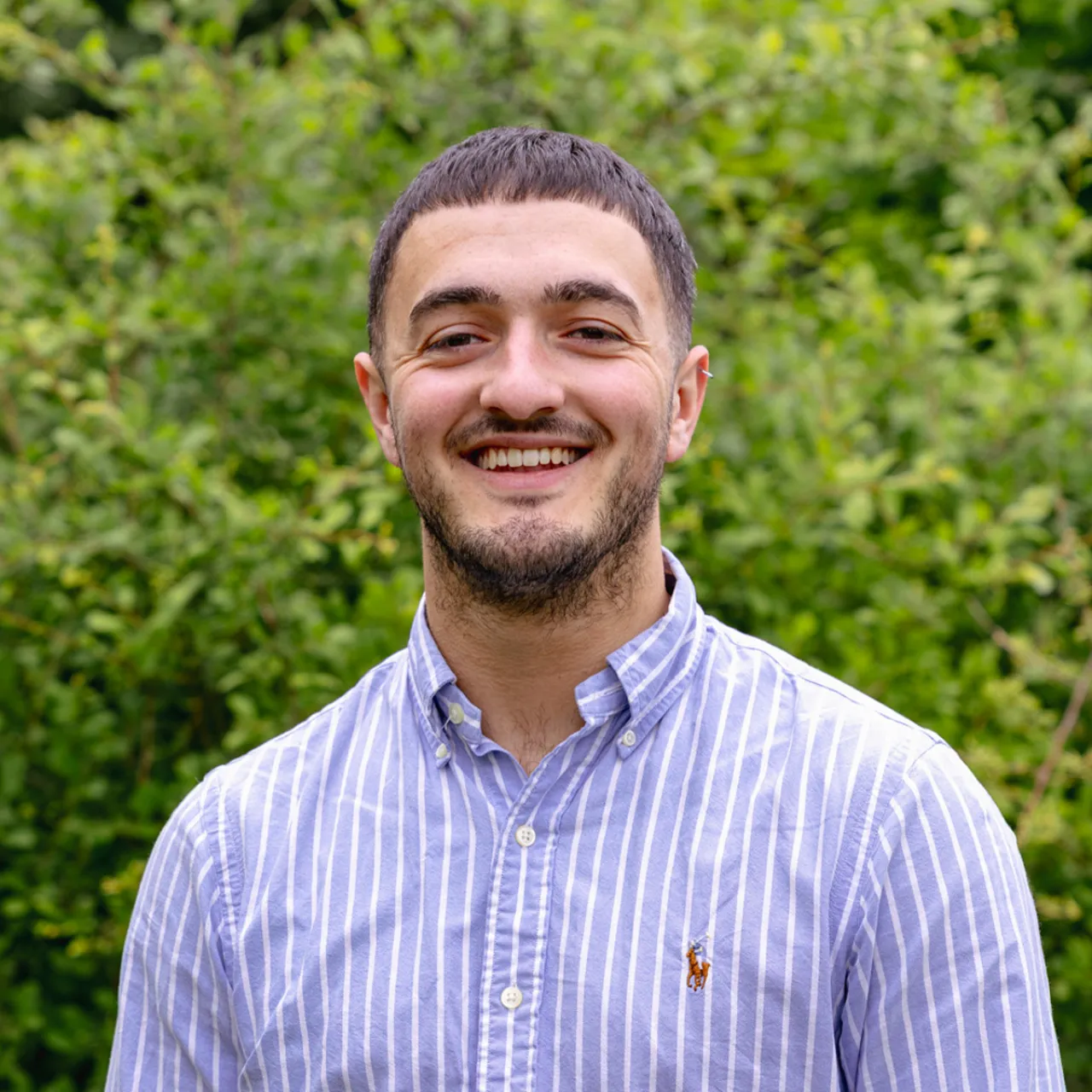 Alfie Hiscock, a young Graduate Landscape Architect at Gillespies' Leeds studio, standing in front of a leafy background