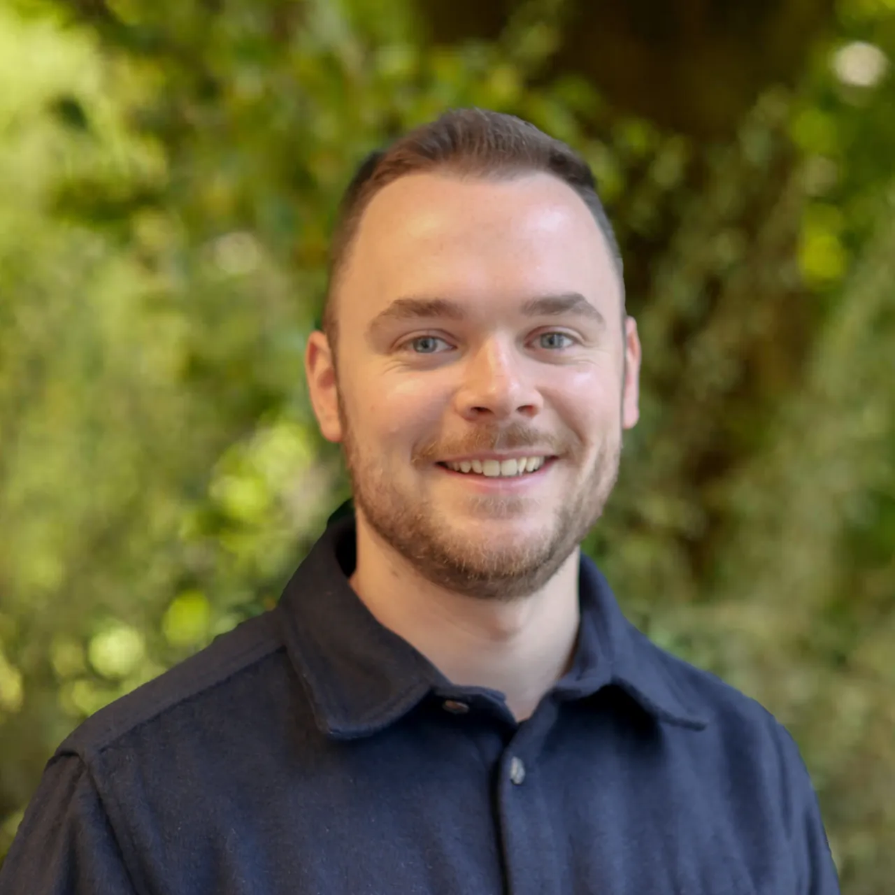 Senior Architect and Urban Designer Justin Smallwood smiles in front of a green wall