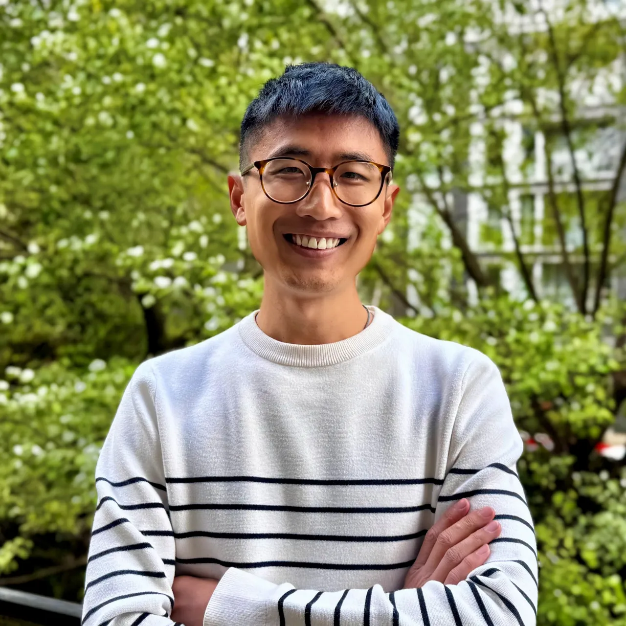 Male in striped jumper and glasses standing in front of green trees